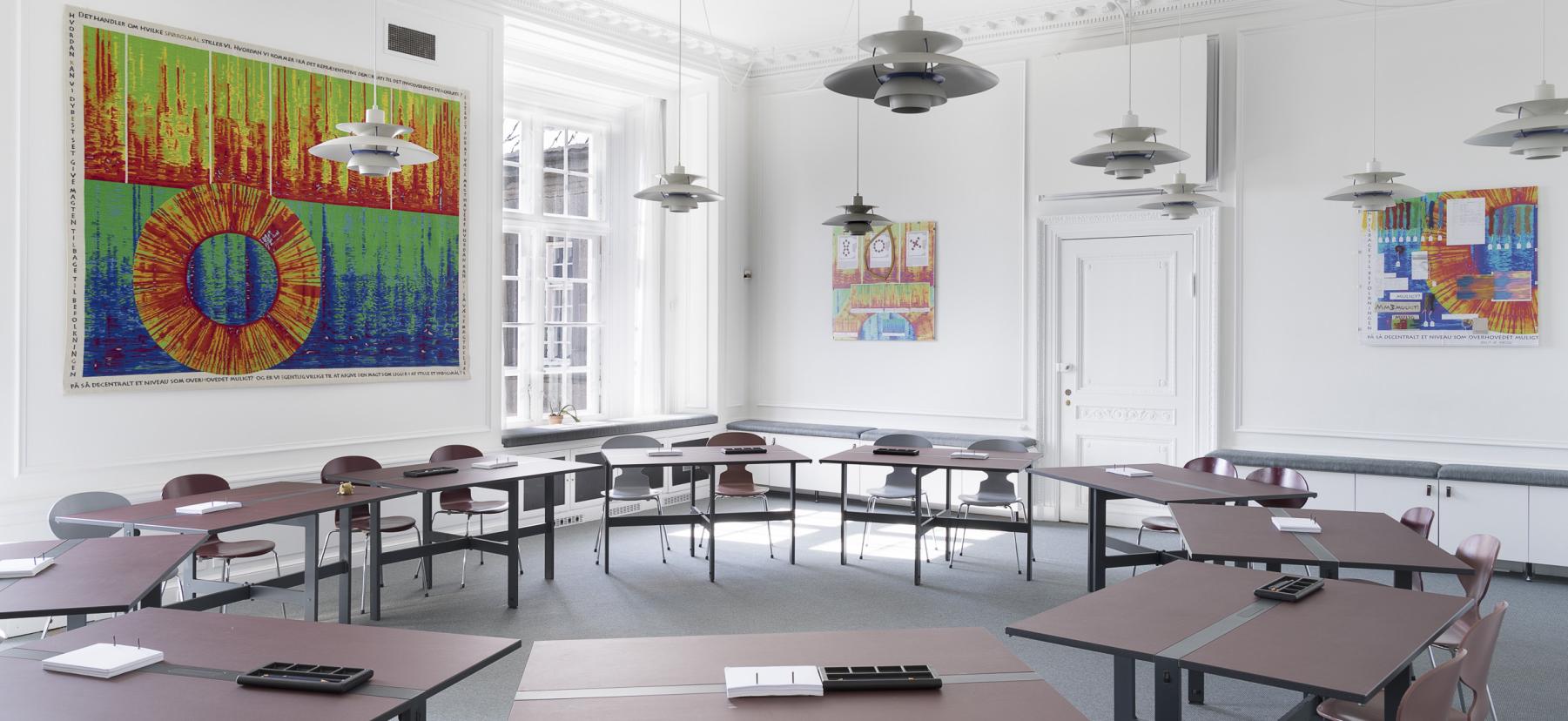 Gruppeværelse med borde i en cirkel og vævet tæppe på væggen