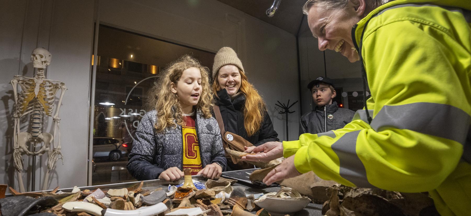 Arkæolog viser potteskår frem til tre personer i Arkæologisk Værksted