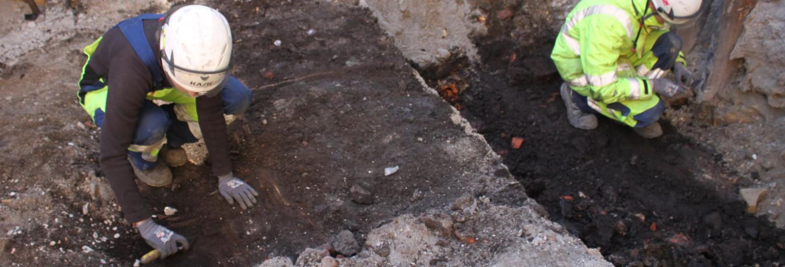 Arkæologer i gang med at grave en træbygget latrinkasse ud, hvis omrids man allerede kan genkende i fladen